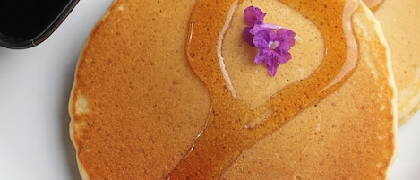 Dos panqueques con jarabe y una flor morada sobre un plato blanco.