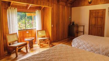 Una habitación de madera con dos camas, una silla de madera, una mesita pequeña y una ventana con cortinas.