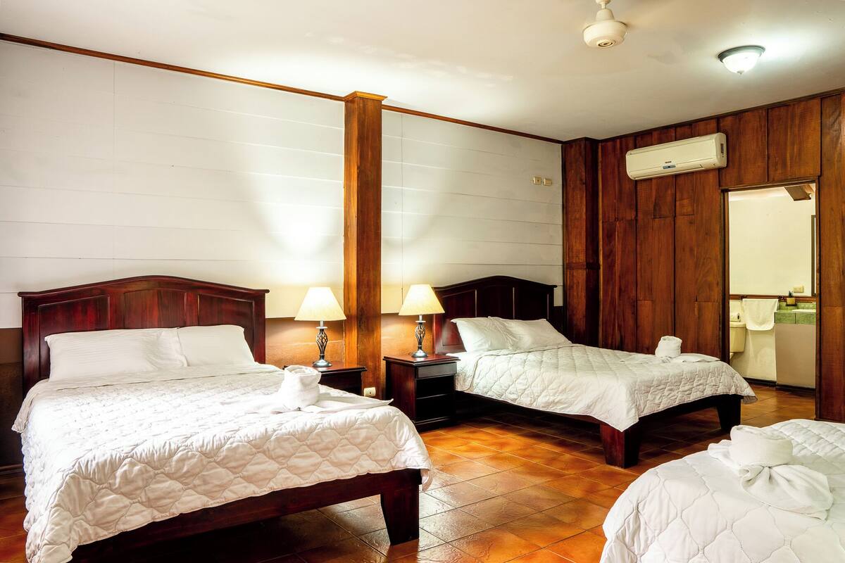 A hotel room with two beds, wooden paneling, and an air conditioning unit.
