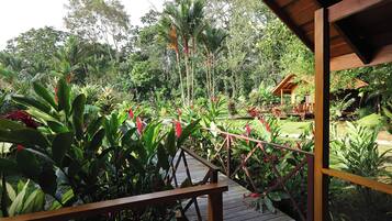 A wooden deck with a railing overlooking a lush garden with various plants and a small structure in the background.