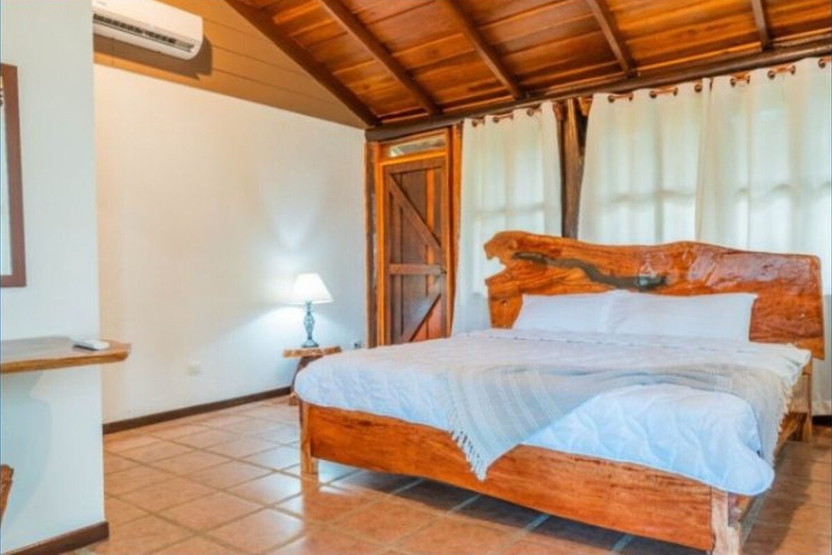 A wooden bed with a headboard, a bedside table with a lamp, and a door with curtains.