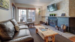 A modern living room with a stone fireplace, leather sofa, and a flat-screen TV mounted on the wall. - Beautiful 1BR Ski-in/Ski-Out on Peak 9 (Breckenridge)