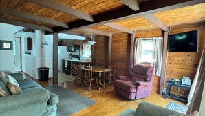 A spacious living area with a wooden ceiling, a dining table with chairs, a sofa, and a television mounted on the wall. - Sunnyside Lake Home at Conneaut Lake (Conneaut Lake)