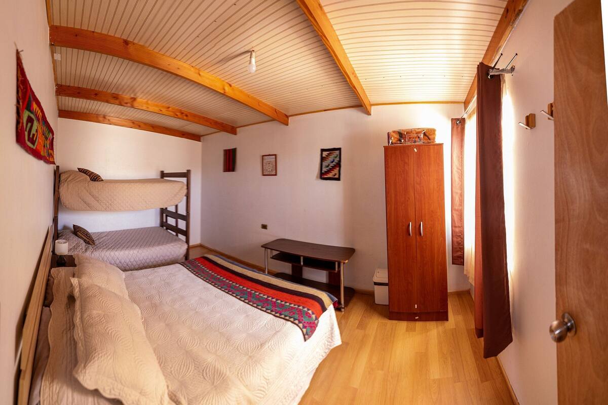 Un dormitorio con una cama doble, una cama individual, un armario de madera y una mesita pequeña.