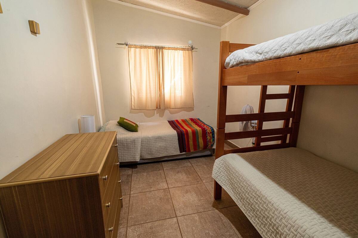 Habitación tipo dormitorio con dos literas, un aparador de madera, una ventana con cortinas y suelo de baldosas.