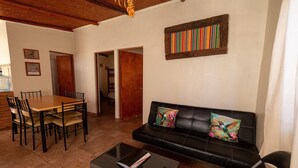 A living room with a black leather sofa, a dining table with chairs, and a coffee table. - Casa Sutar 3 y 4 (San Pedro de Atacama)