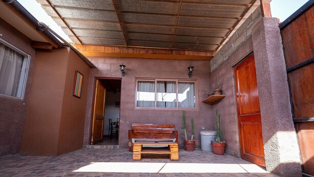A covered patio area with a wooden bench, potted plants, and a wooden door. - Casa Sutar 3 y 4 (San Pedro de Atacama)