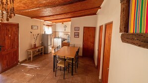 A dining area with a wooden table and chairs, a kitchen in the background, and a wooden ceiling. - Casa Sutar 3 y 4 (San Pedro de Atacama)