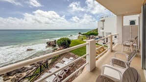 Een balkon met uitzicht op de oceaan, buitenmeubilair en een gazon.