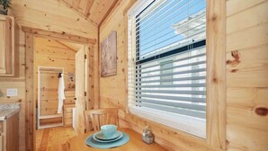 L’intérieur d’une cabane en bois comprend un coin repas, une fenêtre avec des stores et une porte qui donne sur une autre pièce.