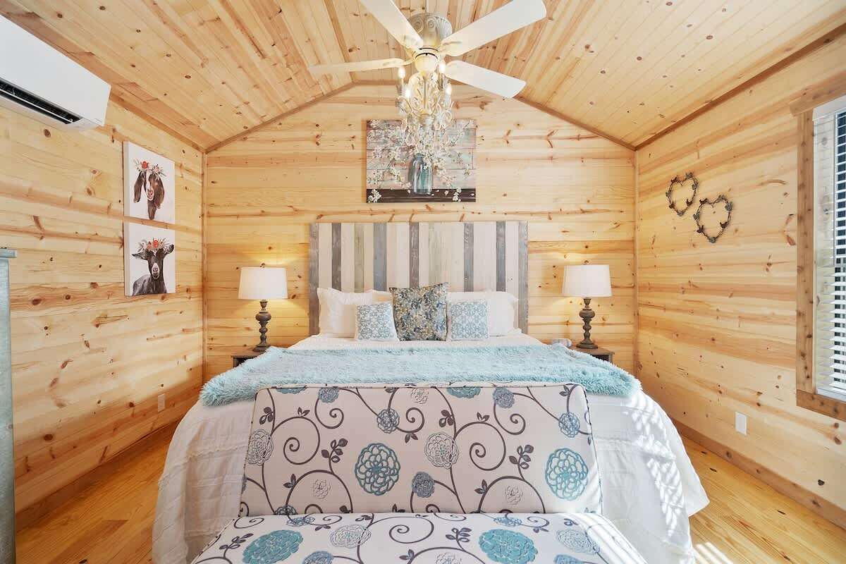 Quarto de cabana de madeira com cama, duas luminárias de cabeceira, um lustre e decorações nas paredes.