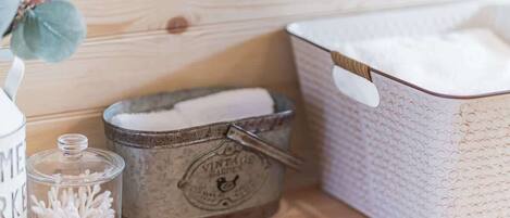 A wooden shelf with a vintage garden-themed tin, a glass jar with cotton swabs, and a white basket with a textured pattern.