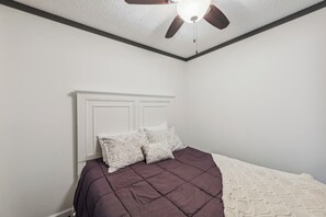 Une chambre à coucher avec un lit, des murs blancs, un ventilateur de plafond et une tête de lit blanche.