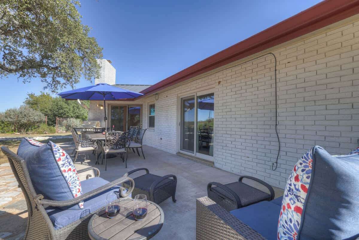 Een terras buiten met rieten meubels, een tafel en een blauwe parasol.