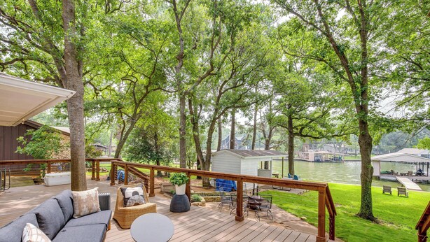 Una terraza de madera con mobiliario exterior, vista a un río y un cobertizo pequeño al fondo.