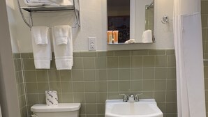 Un bagno compatto con WC, lavandino e vasca da bagno. Asciugamani su un ripiano sopra il WC e un cestino della spazzatura accanto al lavandino.
