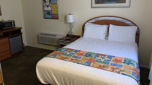 Una camera d'albergo con un letto, una scrivania con un forno a microonde, un termosifone e un quadro appeso al muro.
