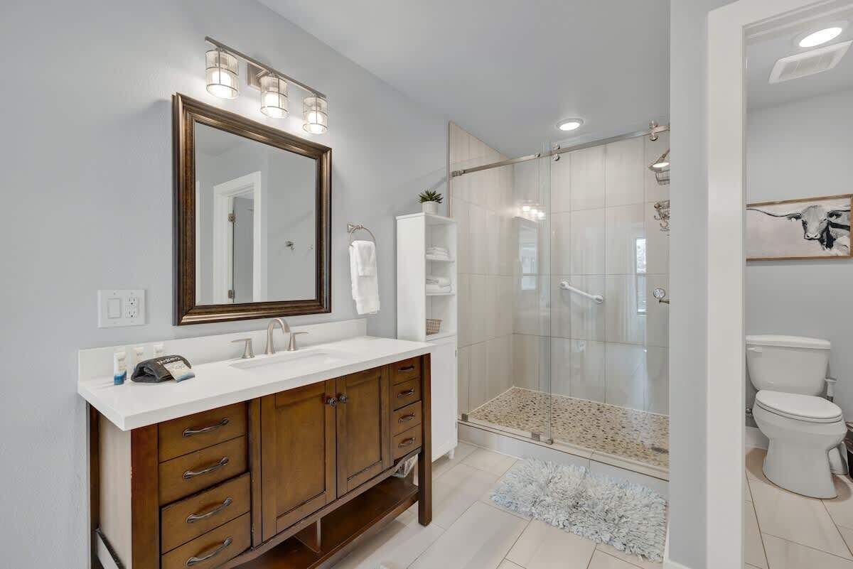 A modern bathroom with a large mirror, double sinks, and a glass-enclosed shower.