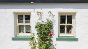 Ein weißes Gebäude mit zwei Fenstern und einer Kletterpflanze mit roten Blüten.