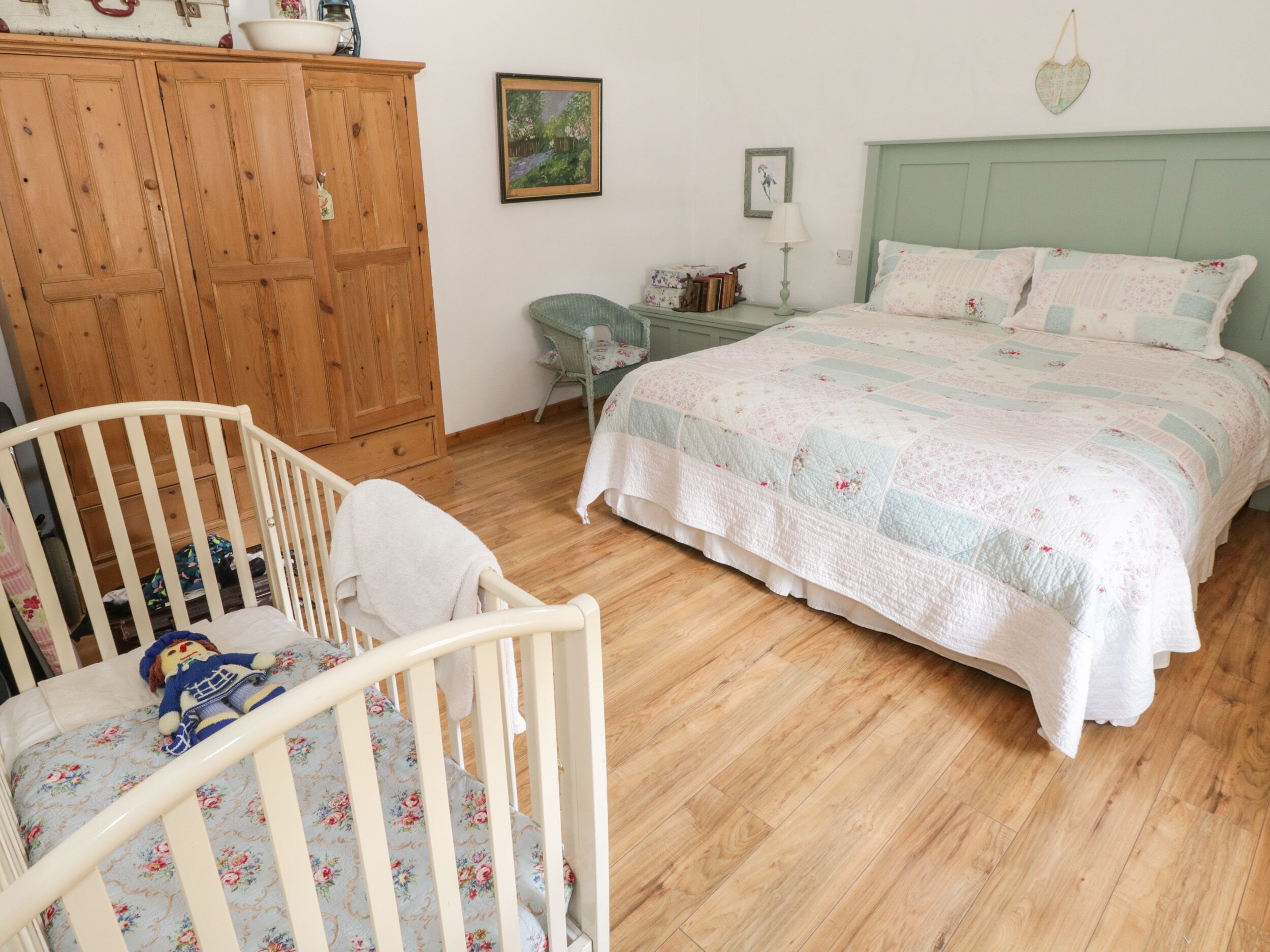 Een slaapkamer met een ledikant, een bed met een bloemenquilt, een houten garderobe en een bureau met een lamp.