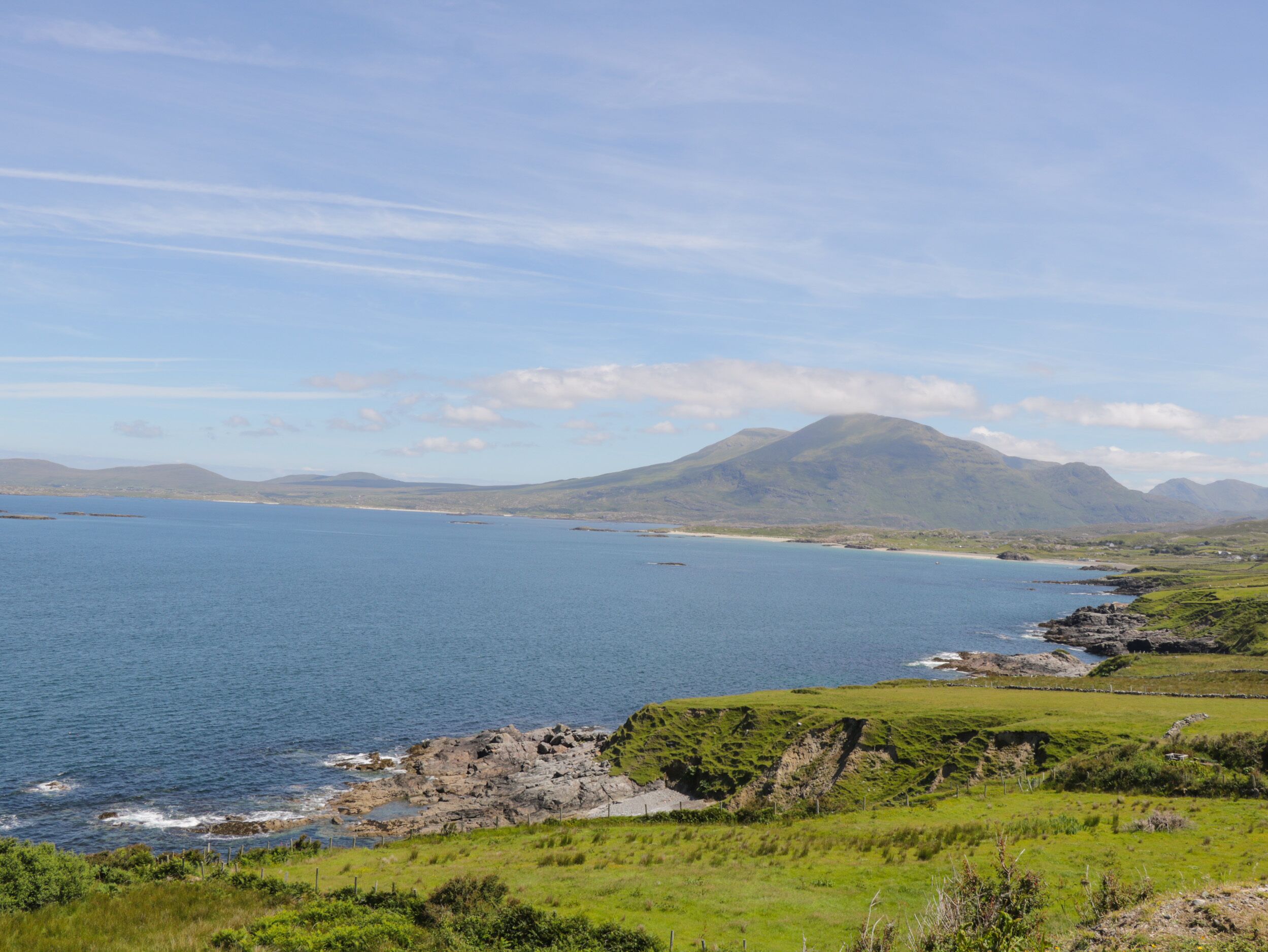 A coastal landscape with a large body of water, green hills, and a mountain in the background.