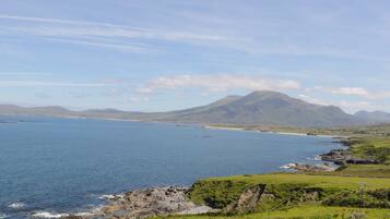 A coastal landscape with a large body of water, green hills, and a mountain in the background.