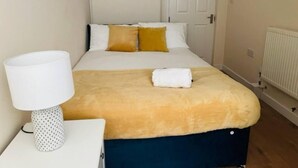 A neatly made bed with a white and yellow duvet, a white lamp on a bedside table, and a white door in the background. - 4 Bed House - Sleeps 9 - Garden - Parking - Wifi (Birmingham)
