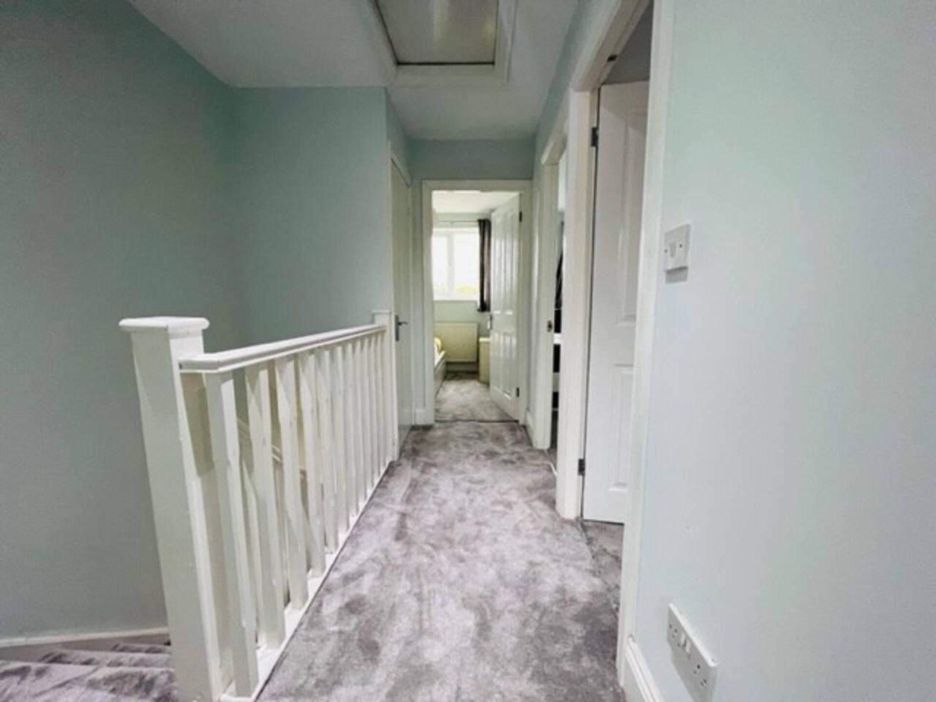 A narrow hallway with a white railing, light green walls, and a gray carpet.