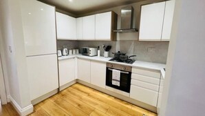 A compact kitchen with white cabinets, a microwave, a stove, and a sink. - 4 Bed House - Sleeps 9 - Garden - Parking - Wifi (Birmingham)