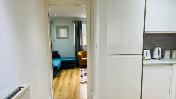 A narrow hallway leading to a bedroom with a bed and a chair, and a kitchen area with cabinets and appliances. - 4 Bed House - Sleeps 9 - Garden - Parking - Wifi (Birmingham)