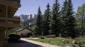A building with a patio area, a mountain view, and a well-maintained garden with trees and shrubs. - Cozy Ketchum Condo  - Walk to Everything! (Ketchum)