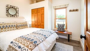 A bedroom with a large bed, a wooden wardrobe, a window with a view, and a wall-mounted mirror. - Cozy Ketchum Condo  - Walk to Everything! (Ketchum)