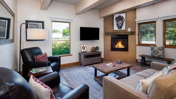 A living room with a fireplace, leather chairs, a sofa, a coffee table, and a TV mounted on the wall. - Cozy Ketchum Condo  - Walk to Everything! (Ketchum)