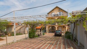 A paved driveway leading to a building with a balcony and a car parked in front. - Apartment at second floor (Pirovac)