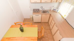 A compact kitchen with a dining area, featuring a sink, cabinets, and a table with chairs. - Apartment at second floor (Pirovac)