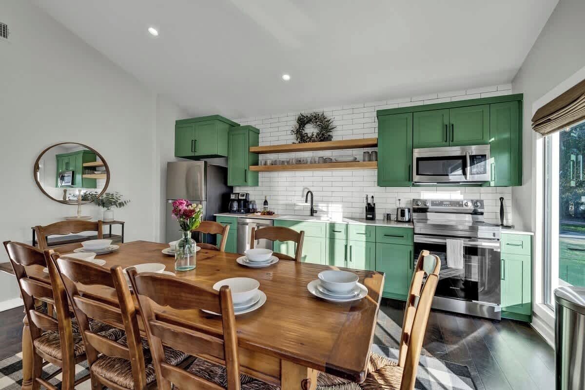 Una cocina moderna con armarios verdes, una mesa de comedor dispuesta con platos y un espejo grande en la pared.