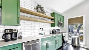 Una cocina moderna con gabinetes verdes, azulejos blancos tipo metro y electrodomésticos de acero inoxidable.