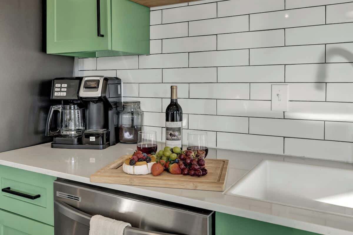 A kitchen with a coffee maker, wine bottle, and fruit on the counter.