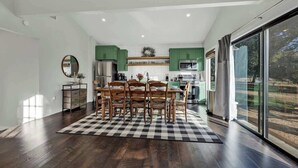 Una cocina moderna con gabinetes verdes, un comedor con alfombra a cuadros y un ventanal con vistas.