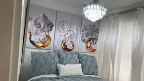 A bedroom with a tufted headboard, a white fluffy bedspread, and three wall-mounted paintings of abstract floral designs. - Sisters Four Bed and Bath - Luxury living in a small town atmosphere!   (Centralia)