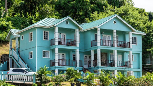 A two-story building with a light blue exterior, multiple balconies, and a staircase leading to the upper floor. - Golden Palms Two-Bedroom Apartment (Diamond)