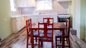 A compact kitchen with white cabinets, a wooden dining table, and patterned chairs. - Golden Palms Two-Bedroom Apartment (Diamond)