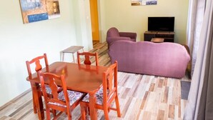 A living room with a purple sofa, a wooden dining table with chairs, and a TV on a stand. - Golden Palms Two-Bedroom Apartment (Diamond)