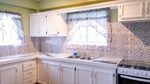 A kitchen with white cabinets, a tiled backsplash, a stove, and a sink. - Golden Palms Two-Bedroom Apartment (Diamond)