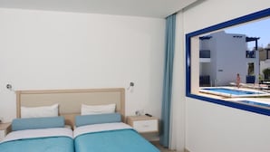 Quarto com uma cama grande, mesa de cabeceira e janela com vista para uma piscina e prédios.
