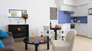 Uma sala de estar moderna com uma mesa de jantar, um sofá e uma área de cozinha com armários brancos e azulejos azuis.