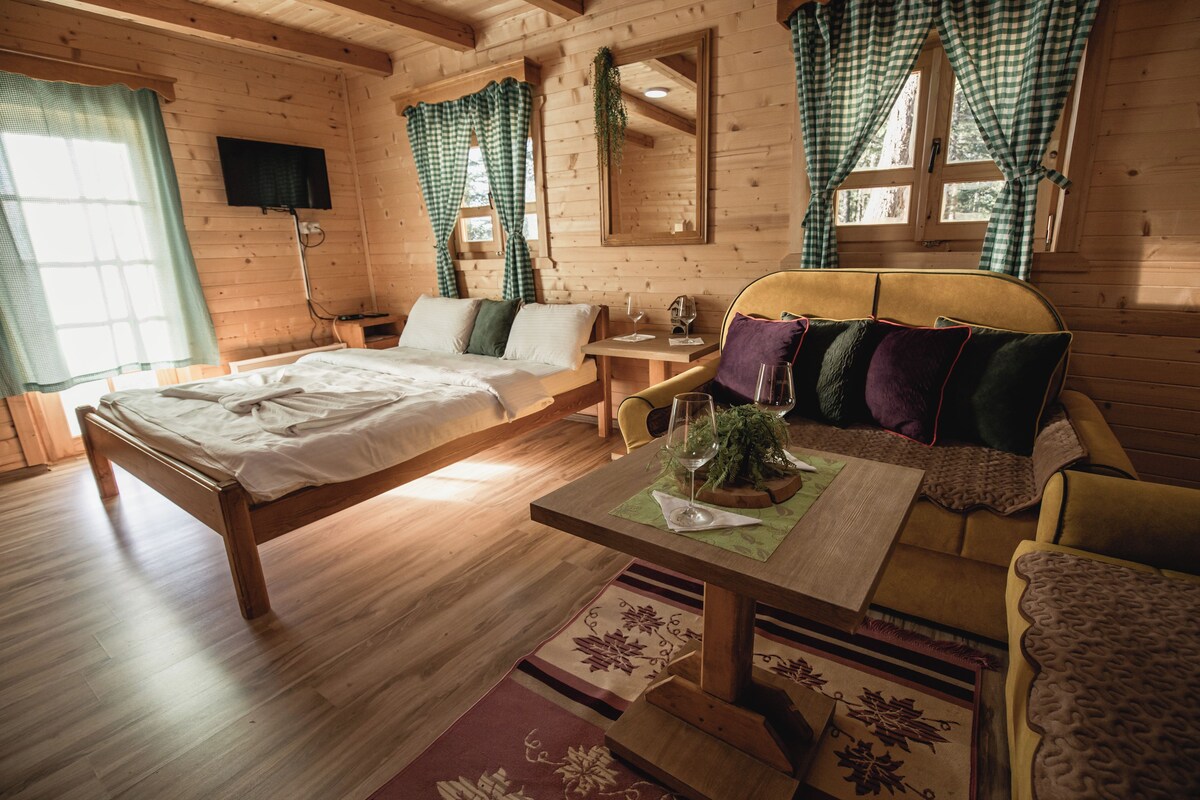 A wooden cabin interior with a bed, sofa, and dining table.