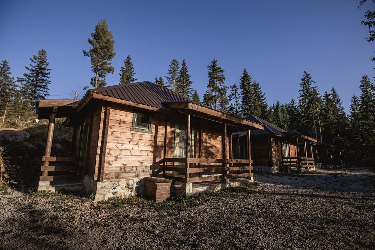 A wooden cabin with a stone foundation, surrounded by a forest.