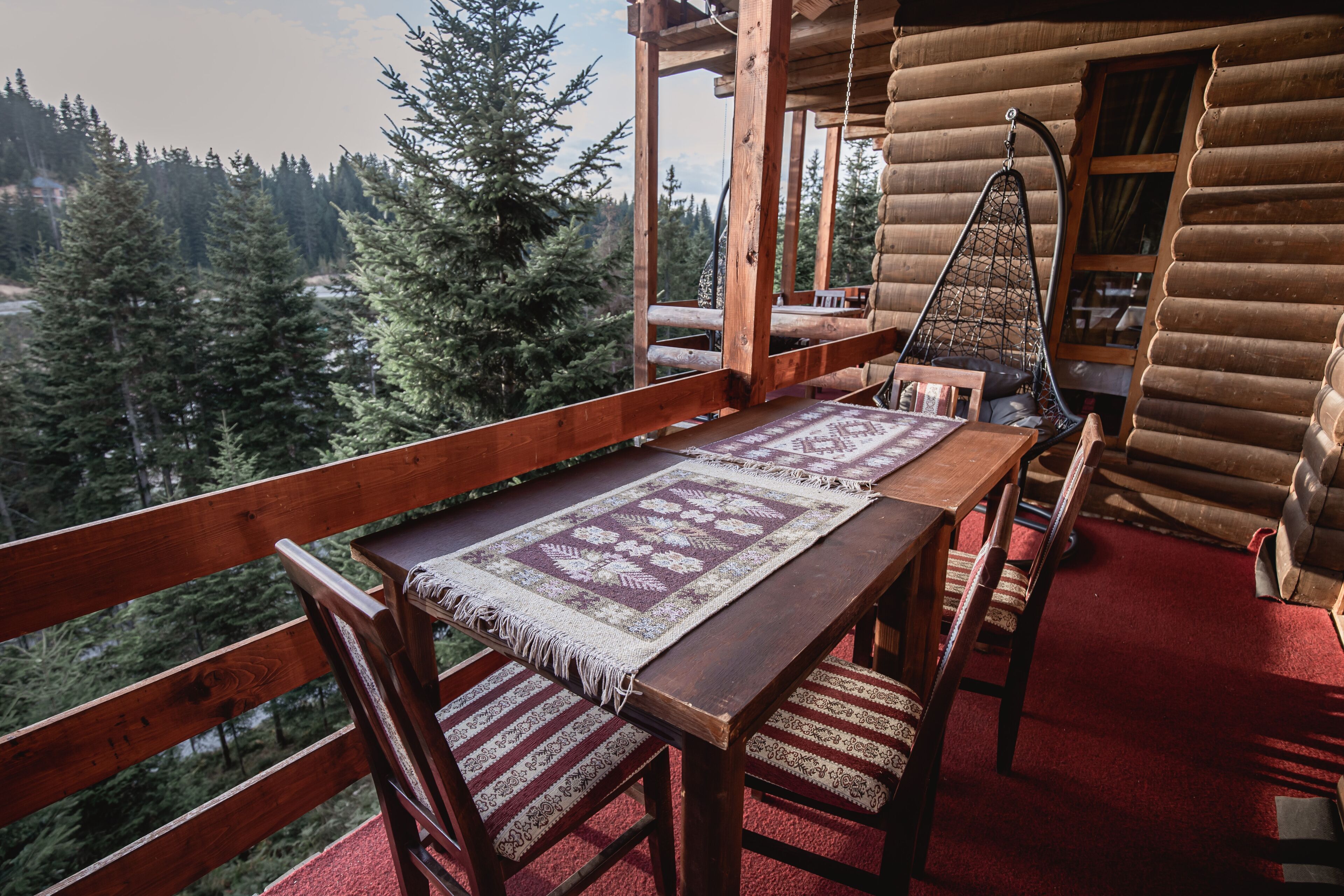 Eine Holzterrasse mit Tisch und Stühlen, einem Hängesessel und Blick auf einen bewaldeten Bereich.