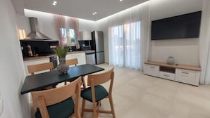 A modern kitchen with a dining area, a flat-screen TV, and a large window with curtains. - Villa Luna 1 with swimming pool in Pitsidia (Pitsidia)